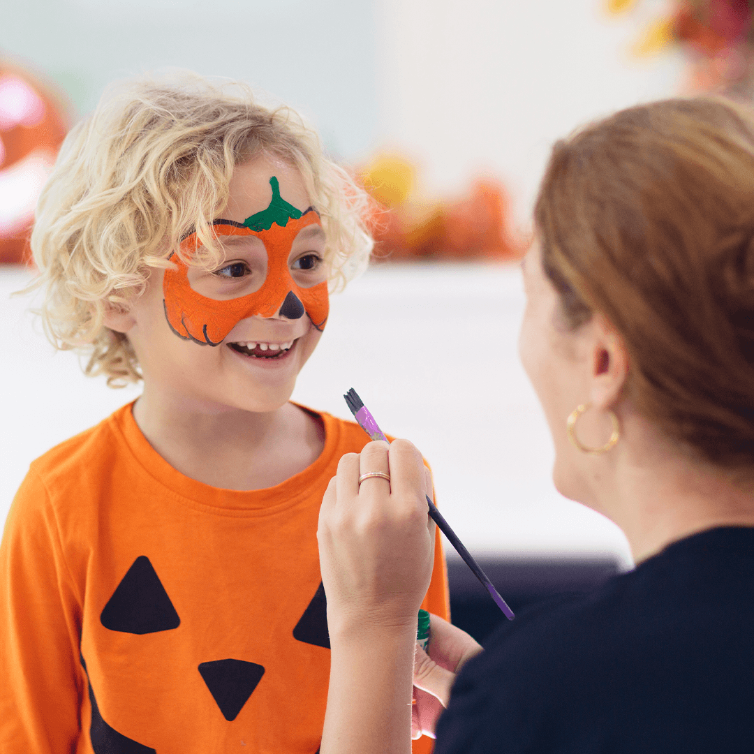 Mor maler et græskarmønster i ansigtet på sin søn til halloween